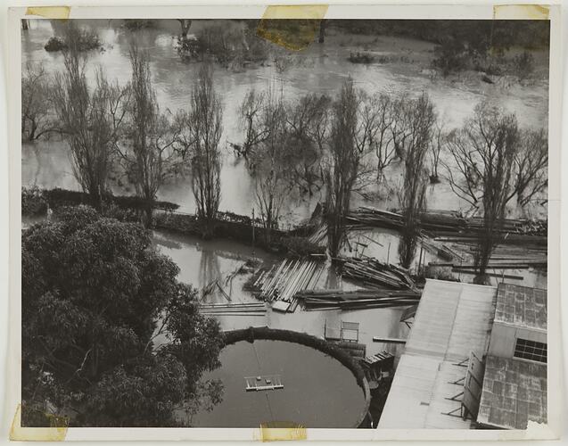 View looking down on flooded river and flood damaged buildings on submerged river bank.