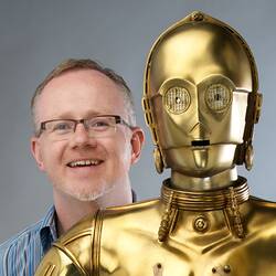 Man with spectacles standing behind gold robot.