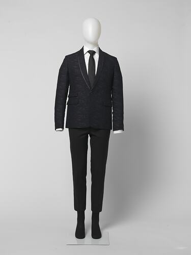 Black suit made of black and grey fabric. Two pockets. White shirt, black tie.