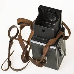 Metal twin lens reflex camera. Body covered in black leather. Leather carry strap. Top view.