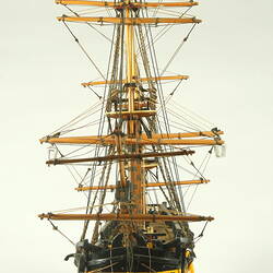 Front view of model ship with wooden hull painted yellow and three masts.