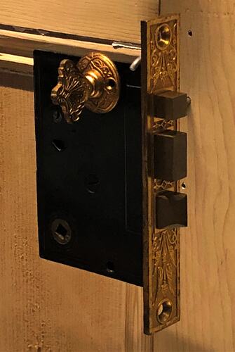 Rectangular metal door lock and latch with gilt faceplate featuring inset decoration. Lock has three bolts.