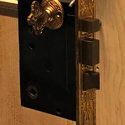 Rectangular metal door lock and latch with gilt faceplate featuring inset decoration. Lock has three bolts.