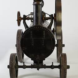 Model of black moveable steam engine on four wheels with tall folded back chimney at front.