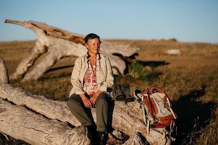 Woman sitting on fallen tree, boots and backpack beside her.