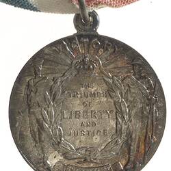 Medal with Australian sailor and soldier supporting a wreath. Text in centre. Loop and ring at top.
