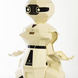 Cream plastic robot with angular human-like shape, ie. head, shoulders, waist and legs. Black plastic features. Arms out.