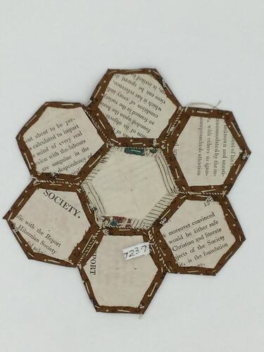 Hexagonal printed card backing for coloured fabric patches that are stitched together.