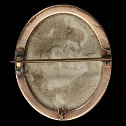 Back of white porcelain brooch with gold setting and horizontal pin.