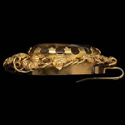 Profile of two part brooch. Top, ornate gold frame with transparent brown cut stone. Below hangs smaller teardrop version