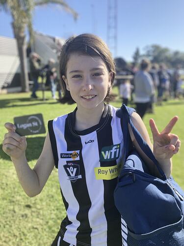 Half portrait, girl wearing black and white striped football jumper. She holds a card is giving a victory sign.