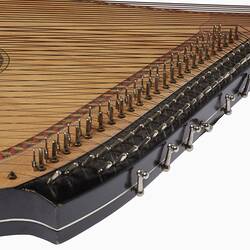 Detail of the base of a timber stringed instrument. Pale wood with black laquered timber detail. Multi stringed.