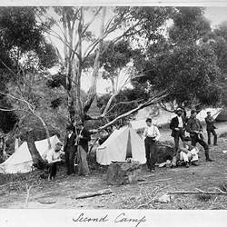 Men gathered around a campsite with canvas tents.