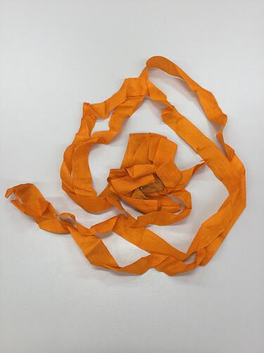 Rosette made from folded and looped bright orange ribbon. Pinned through centre, with a red white and blue ribbon.