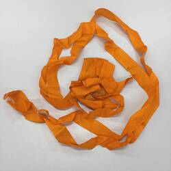 Rosette made from folded and looped bright orange ribbon. Pinned through centre, with a red white and blue ribbon.