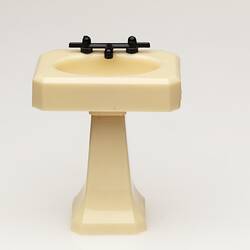 Toy bathroom sink made of cream coloured moulded plastic. Two faucets.