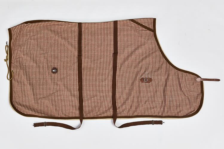 Rectangular woollen horse rug, brown and white check. Brown fastenings and leather straps. Folded, right side.