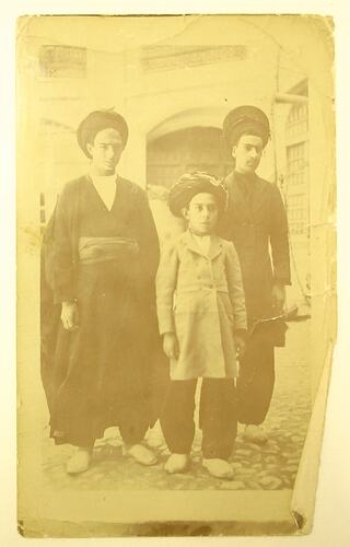 Two Arab men and boy standing outside a building.
