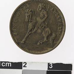 Round medal with man on horseback and text surrounding.