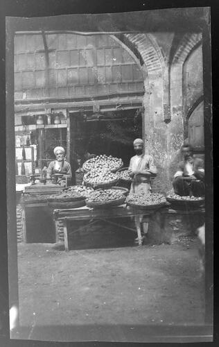 Three turbaned men standing in a market produce stall.