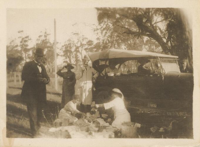 Group of men and woman having picnic next to car.