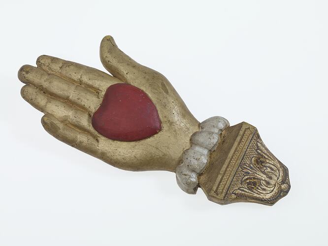 Gold wooden hand with carved red heart on palm. Decorative white and gold cuff.