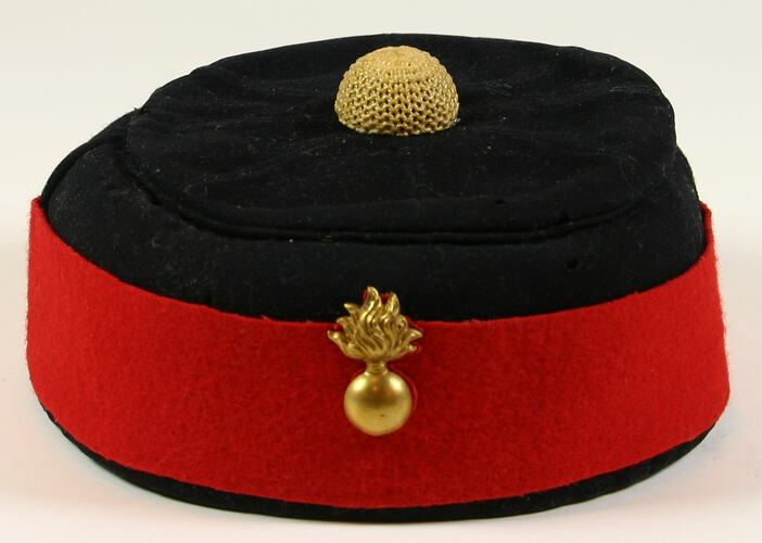 Black wool hat with red wool band and gold broach around rim and yellow decoration on top centre.