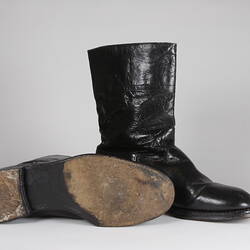 Pair of black leather boots, one boot standing upright, one boot on its side showing sole.