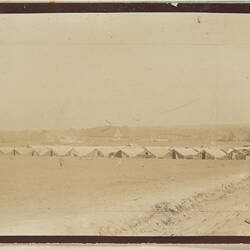 Clear land in foreground, row of twelve tents in midground, town in background.