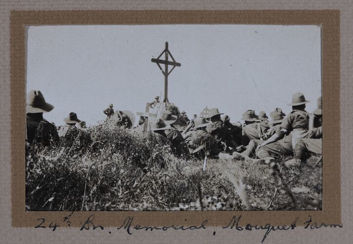 Soldiers gathered around cross, sitting in grass.