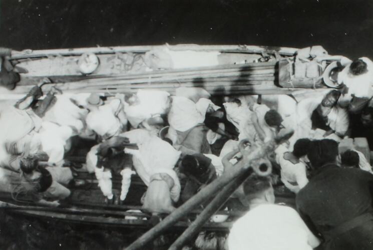 View from above of a lifeboat with passengers alongside a larger ship.