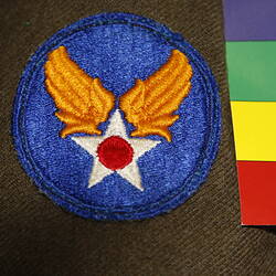 Detail, blue circular cloth badge on khaki fabric. Features gold wings on white star with red central circle.