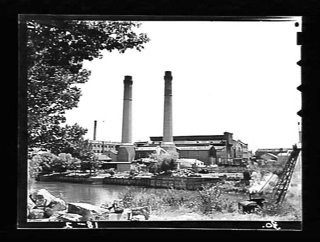 Power station with two central chimneys. River in foreground.