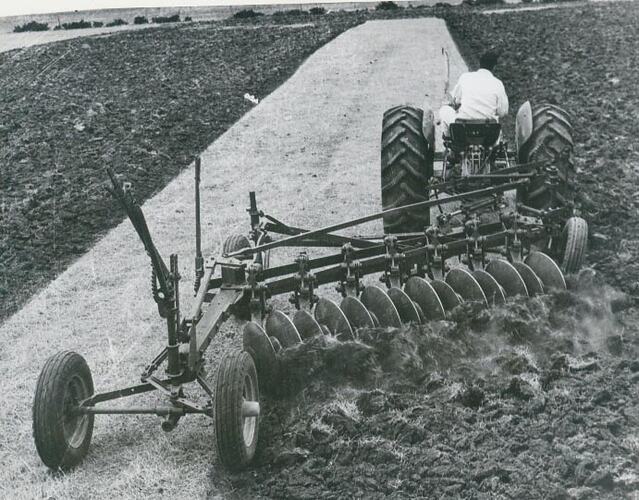 Rrear view of a man driving a tractor coupled to a plough through a field.