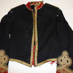 Black military uniform jacket with gold embroidery around edges and cuffs and red collar, front view.