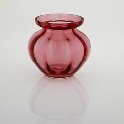 Pink glass vase with reflection below on a shiny white surface.
