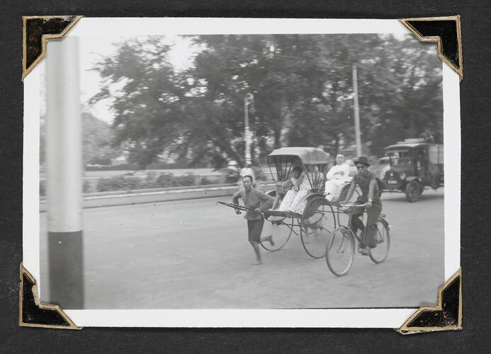 Rickshaw with runner and passengers and a bicycle rider on road.