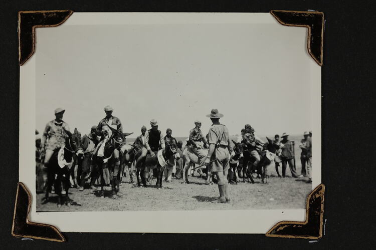 Man standing in front of six men on donkeys, with crowed of people behind.