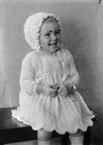 Female toddler in knitted dress and bonnet.