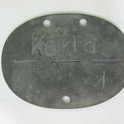 Oval shaped metal disc with dividing line down centre and inscribed text.