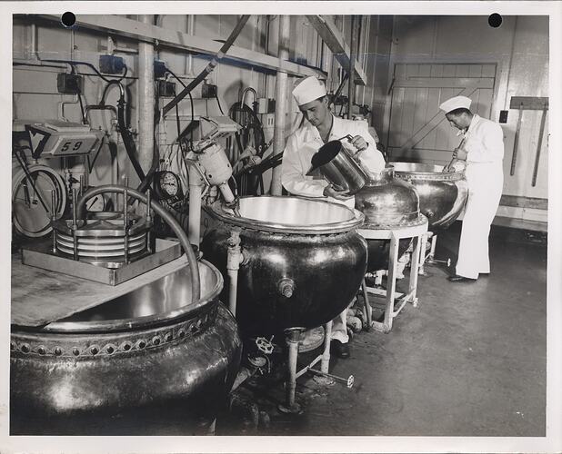 Two men working at large factory kettles.