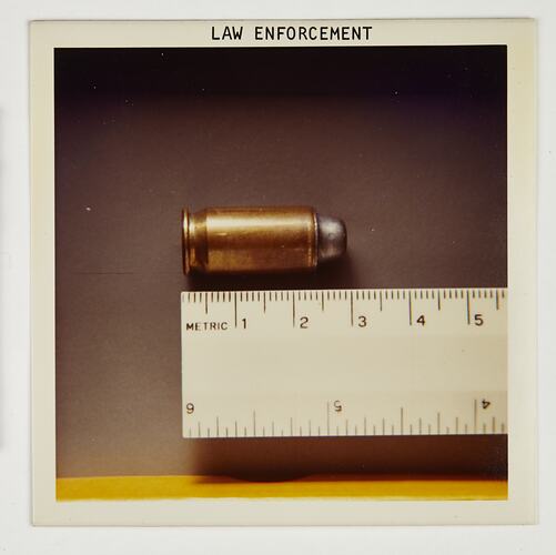 Bullet in cartridge against metal ruler.