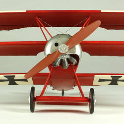 Red aeroplane model. White strip on top of wings with black cross. Front view.