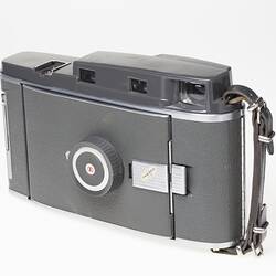 Grey steel camera with silver trim, collapsible bellows and leather handle. Front cover closed.