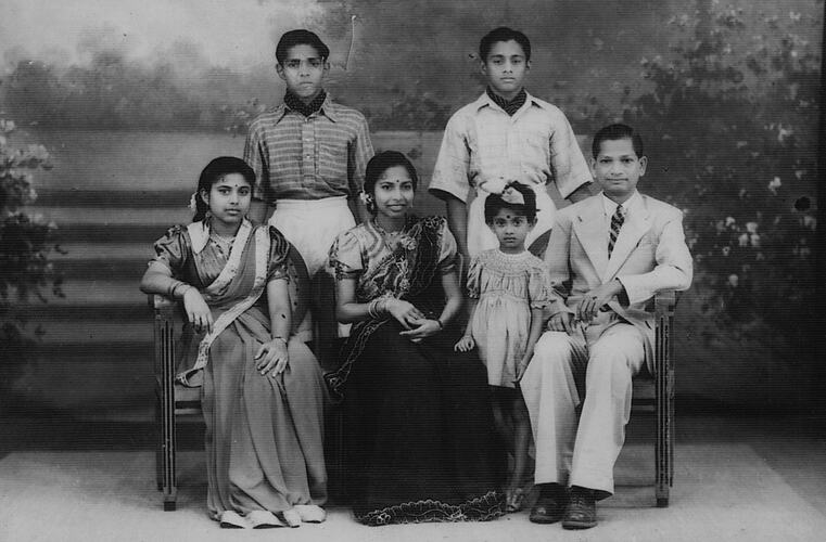 Group of seated and standing people against painted garden backdrop.