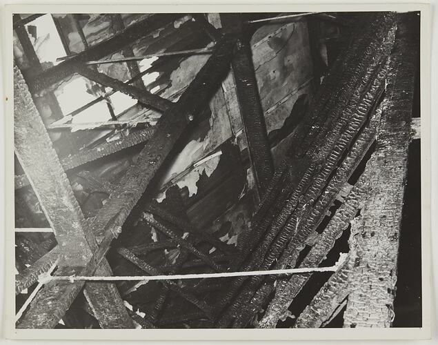 Looking up at interior of burnt roof with charred beams visible.