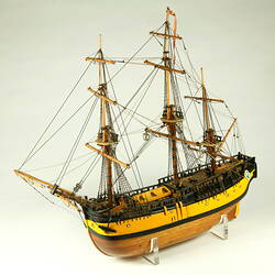 Three quarter view of model ship with wooden hull painted yellow and three masts.