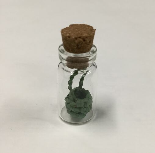 Miniature basket in glass phial with cork stopper.