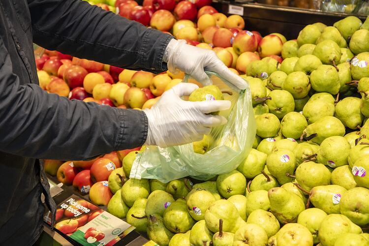 Gloved hands putting pears in plastic bag.