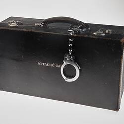 Black leather briefcase marked 'Attache Case' with handcuffs on the handle.